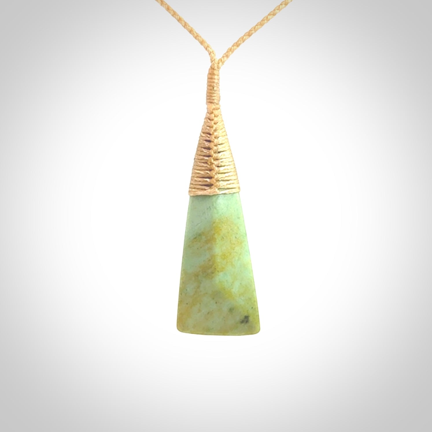 This photo shows a medium sized jade drop shaped pendant. It a a lovely varied green and light orange New Zealand Flower jade. The cord is a four plait beige and is adjustable in length.