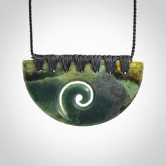 This picture shows a hand carved jade half-shield with Koru pendant. The cord is hand plaited and adjustable so that you can position the pendant where it suits you best.