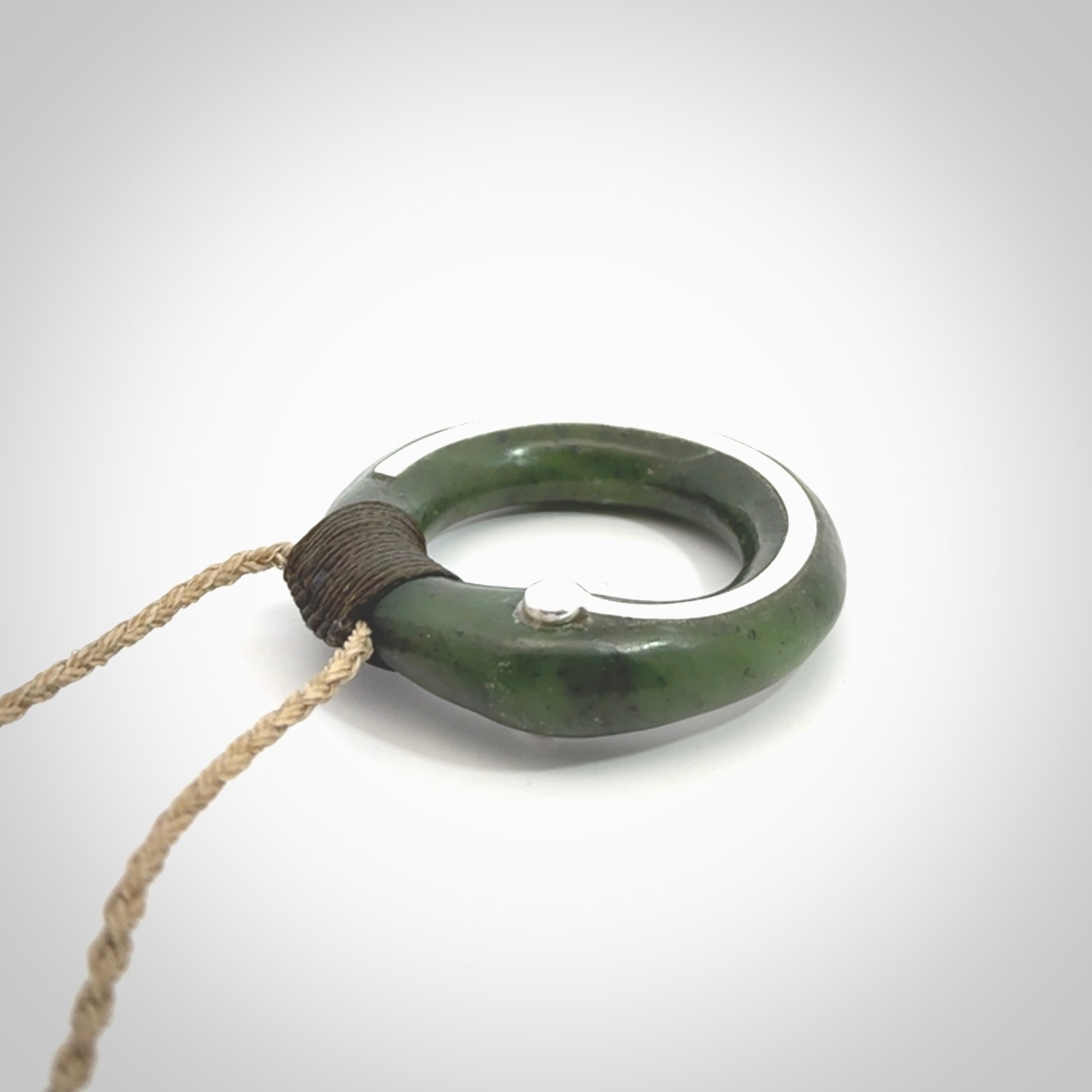 This picture shows a hand carved Nephrite jade circle pendant with sterling silver inlay. It is suspended from an adjustable Kalahari coloured cord. Delivery is free worldwide.