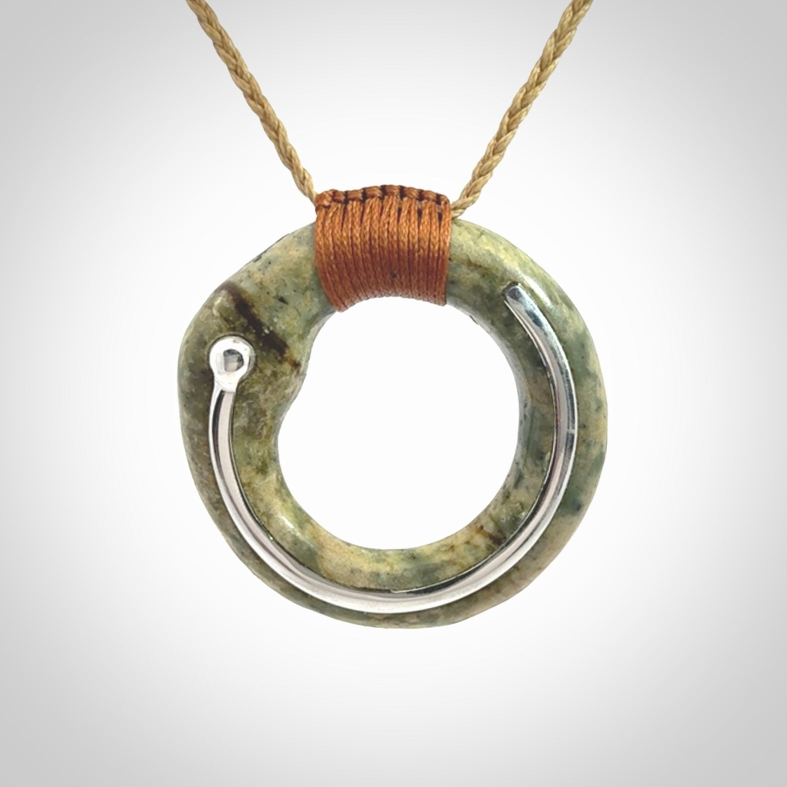 This picture shows a hand carved Nephrite jade circle pendant with sterling silver inlay. It is suspended from an adjustable coloured cord. Delivery is free worldwide.