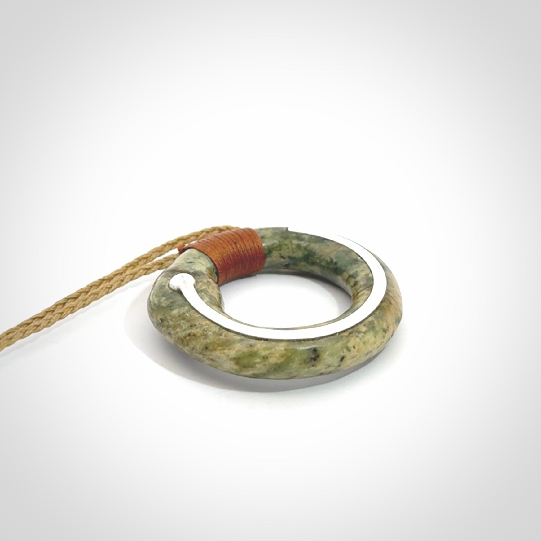 This picture shows a hand carved Nephrite jade circle pendant with sterling silver inlay. It is suspended from an adjustable coloured cord. Delivery is free worldwide.