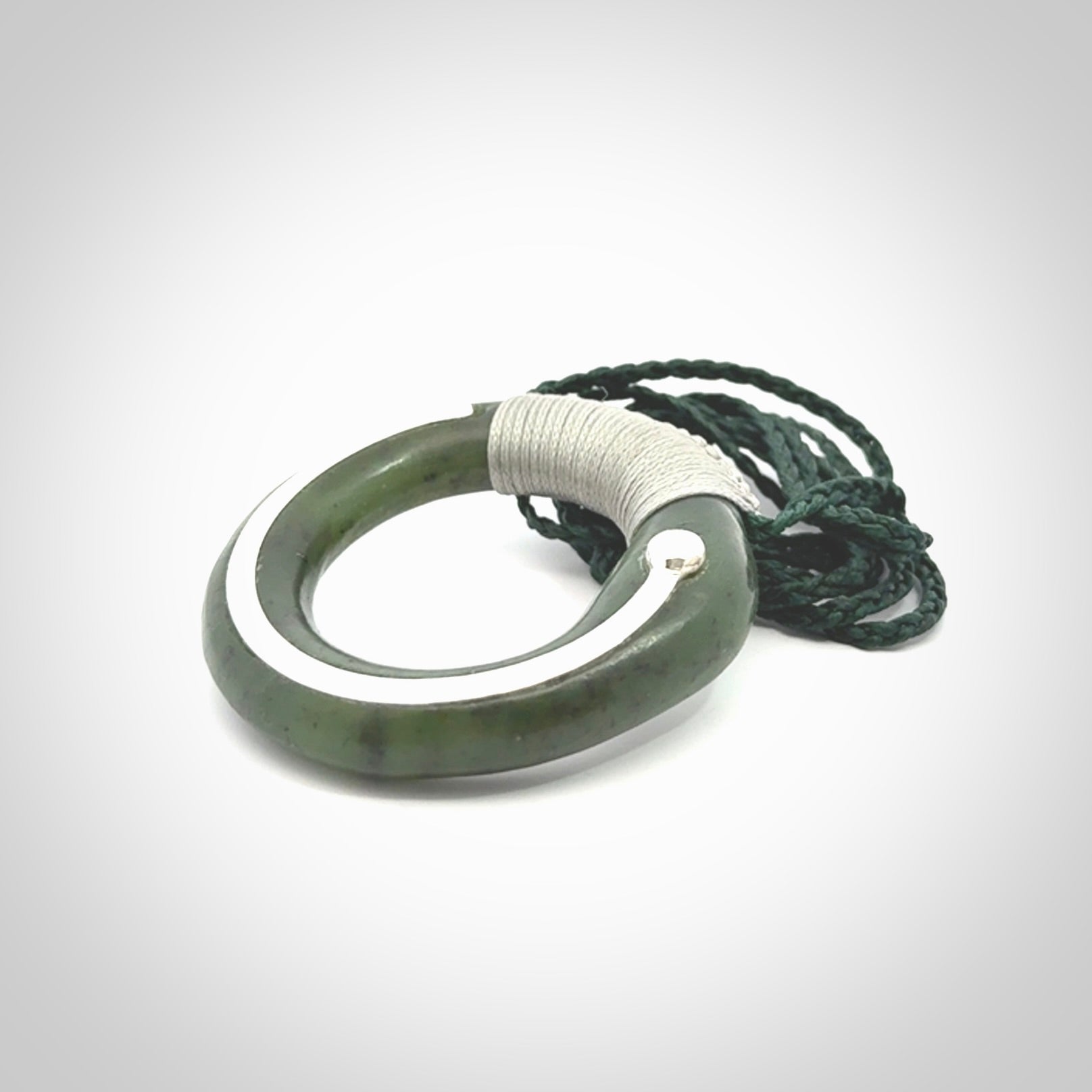 This picture shows a hand carved Nephrite jade circle pendant with sterling silver inlay. It is suspended from an adjustable coloured cord. Delivery is free worldwide.