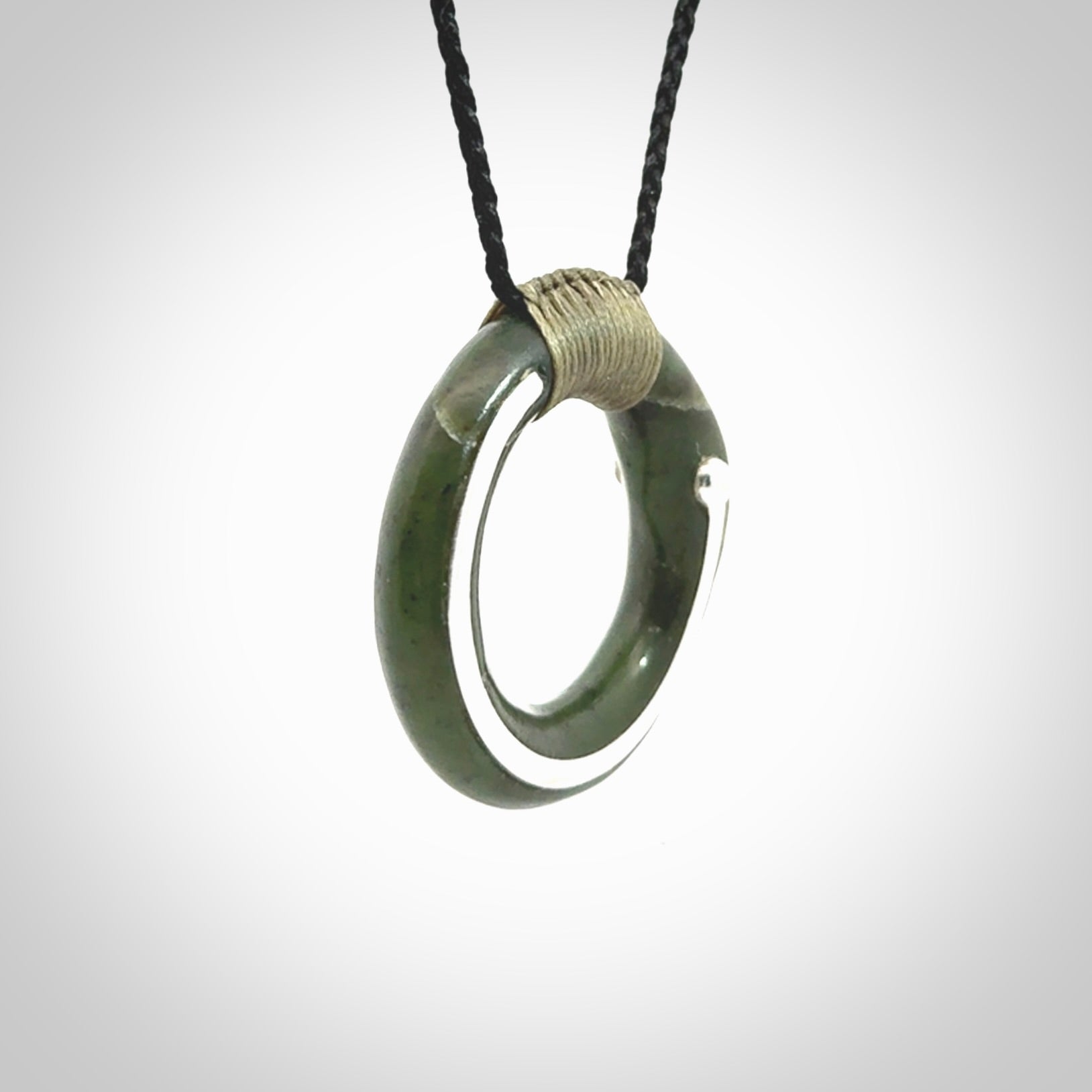 This picture shows a hand carved Nephrite jade zen circle pendant with sterling silver inlay. It is suspended from an adjustable cord.