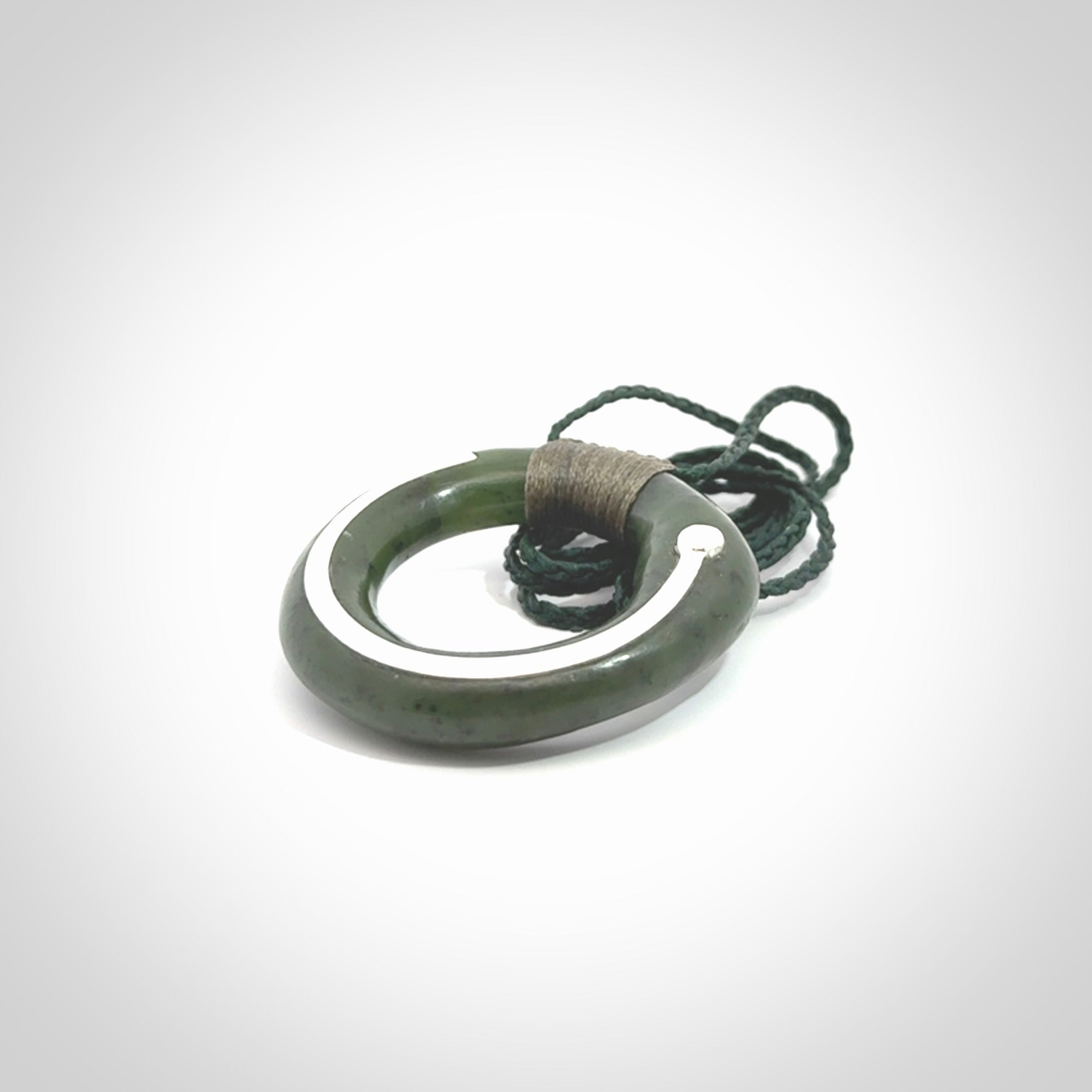 This picture shows a hand carved Nephrite jade zen circle pendant with sterling silver inlay. It is suspended from an adjustable cord.