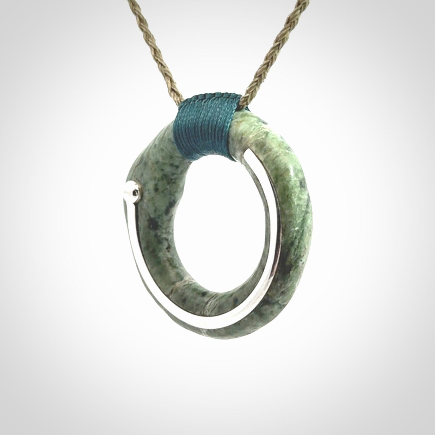 This picture shows a hand carved Nephrite jade circle pendant with sterling silver inlay. It is suspended from an adjustable coloured cord. Delivery is free worldwide.