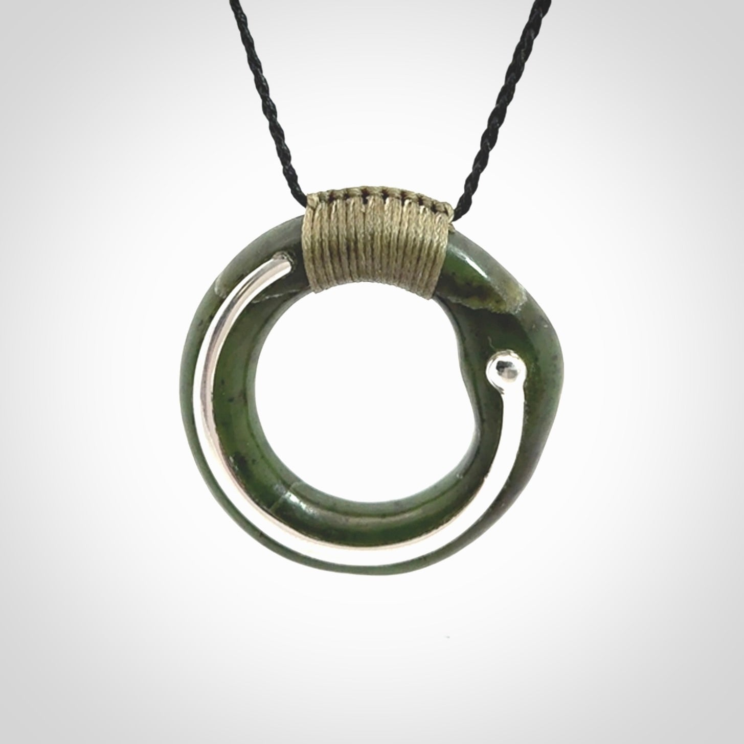 This picture shows a hand carved Nephrite jade zen circle pendant with sterling silver inlay. It is suspended from an adjustable cord.