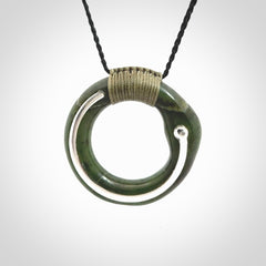 This picture shows a hand carved Nephrite jade zen circle pendant with sterling silver inlay. It is suspended from an adjustable cord.