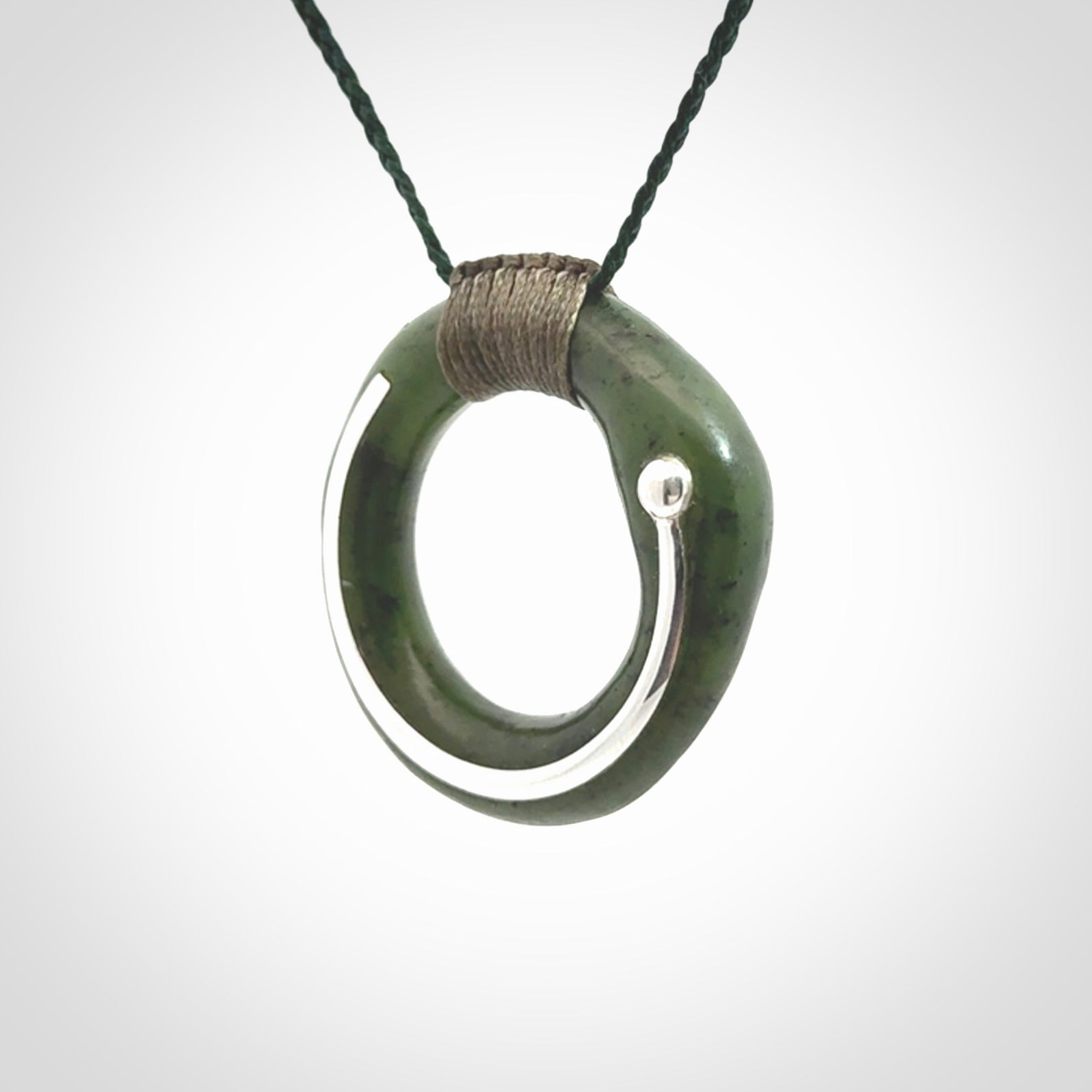 This picture shows a hand carved Nephrite jade zen circle pendant with sterling silver inlay. It is suspended from an adjustable cord.