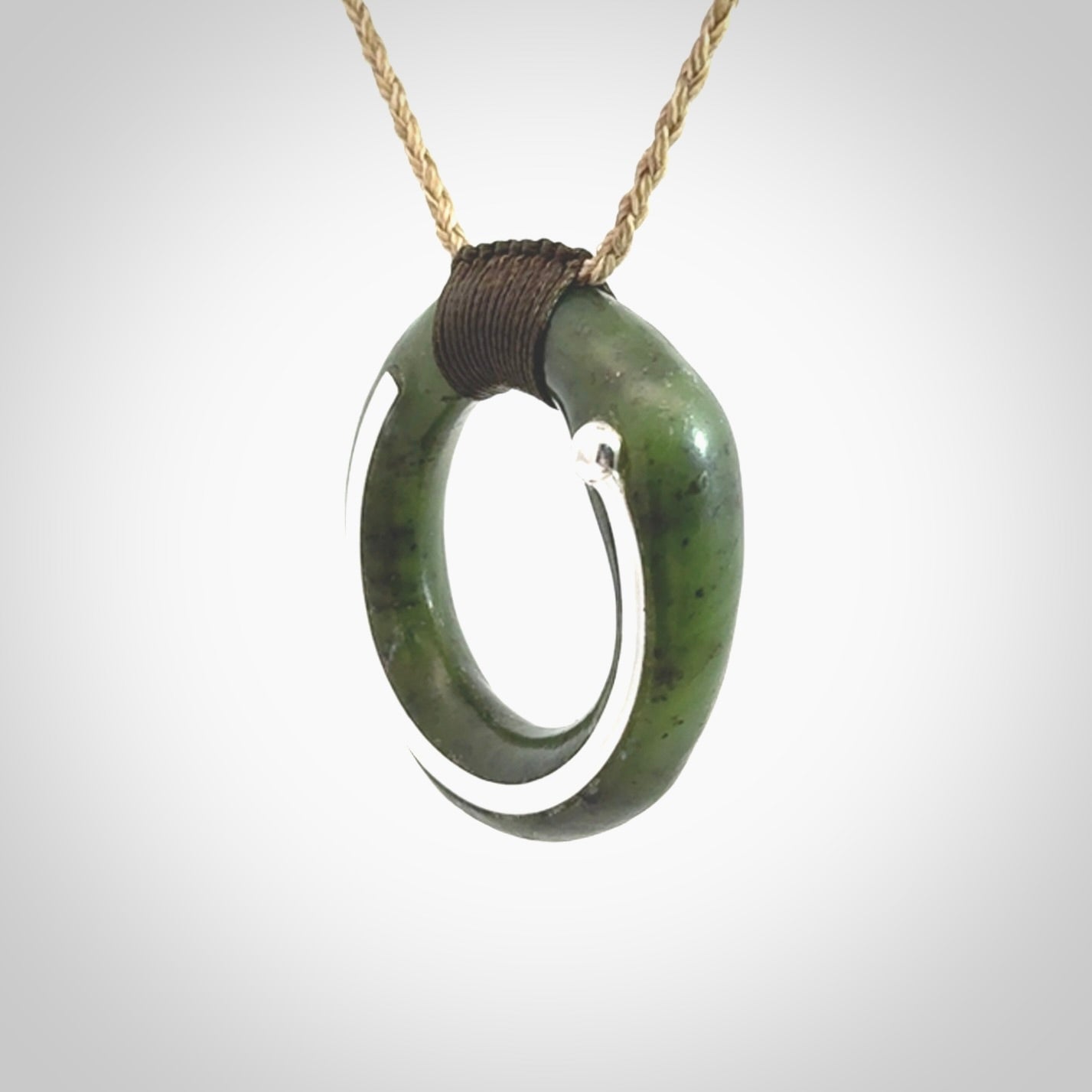 This picture shows a hand carved Nephrite jade circle pendant with sterling silver inlay. It is suspended from an adjustable Kalahari coloured cord. Delivery is free worldwide.