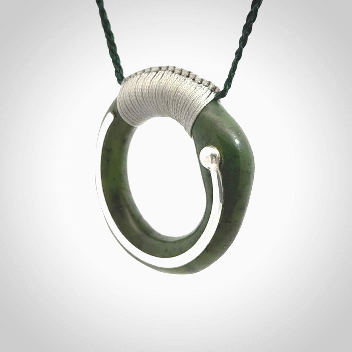 This picture shows a hand carved Nephrite jade circle pendant with sterling silver inlay. It is suspended from an adjustable coloured cord. Delivery is free worldwide.