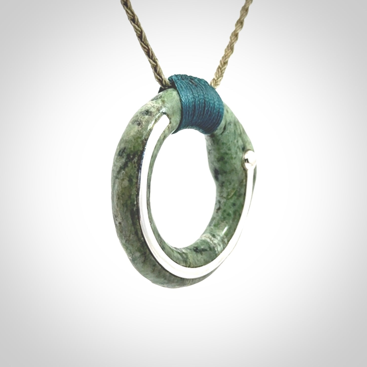 This picture shows a hand carved Nephrite jade circle pendant with sterling silver inlay. It is suspended from an adjustable coloured cord. Delivery is free worldwide.