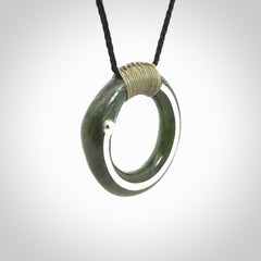 This picture shows a hand carved Nephrite jade zen circle pendant with sterling silver inlay. It is suspended from an adjustable cord.