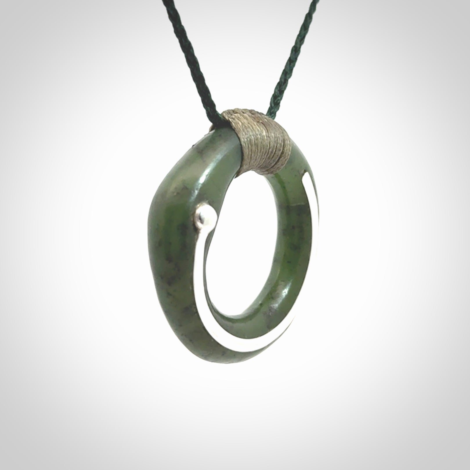 This picture shows a hand carved Nephrite jade zen circle pendant with sterling silver inlay. It is suspended from an adjustable cord.