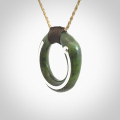 This picture shows a hand carved Nephrite jade circle pendant with sterling silver inlay. It is suspended from an adjustable Kalahari coloured cord. Delivery is free worldwide.