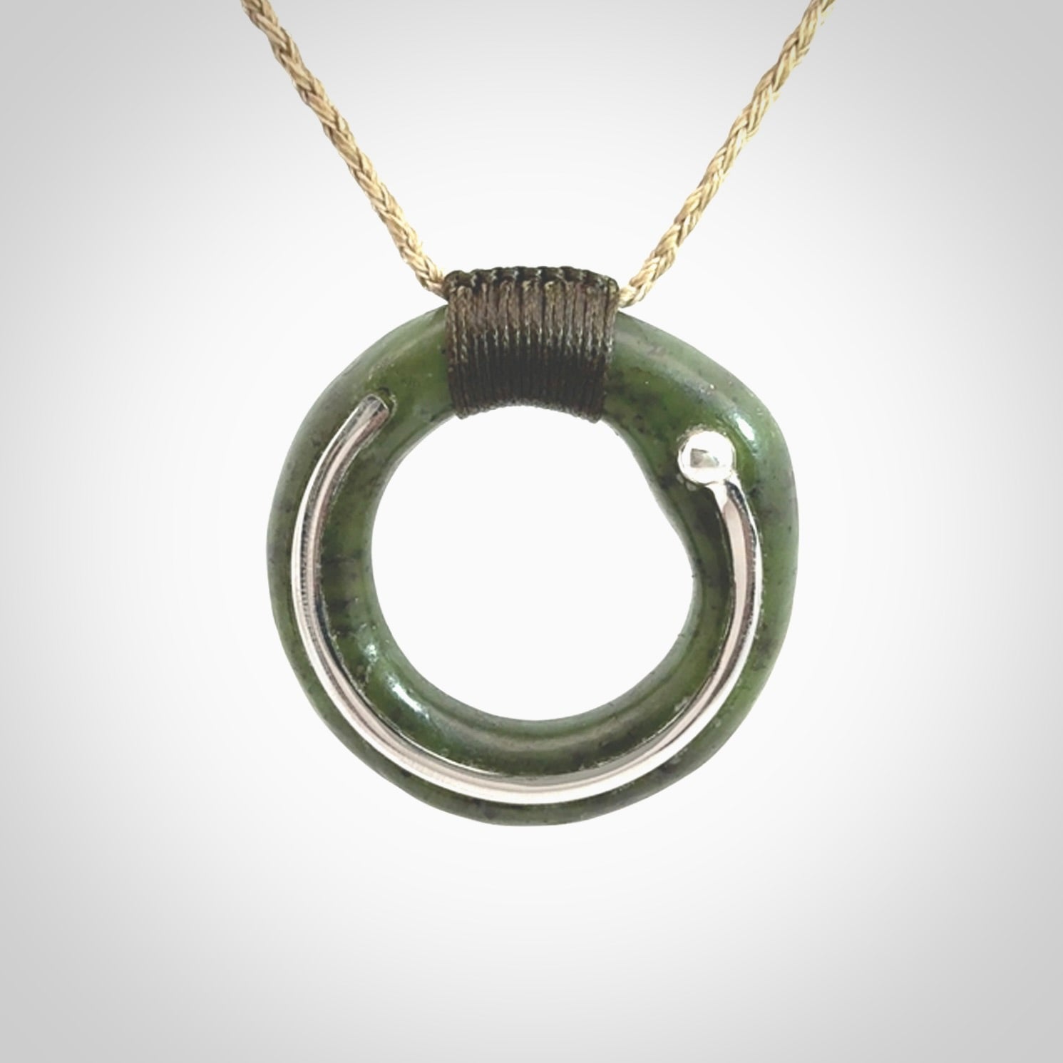 This picture shows a hand carved Nephrite jade circle pendant with sterling silver inlay. It is suspended from an adjustable Kalahari coloured cord. Delivery is free worldwide.