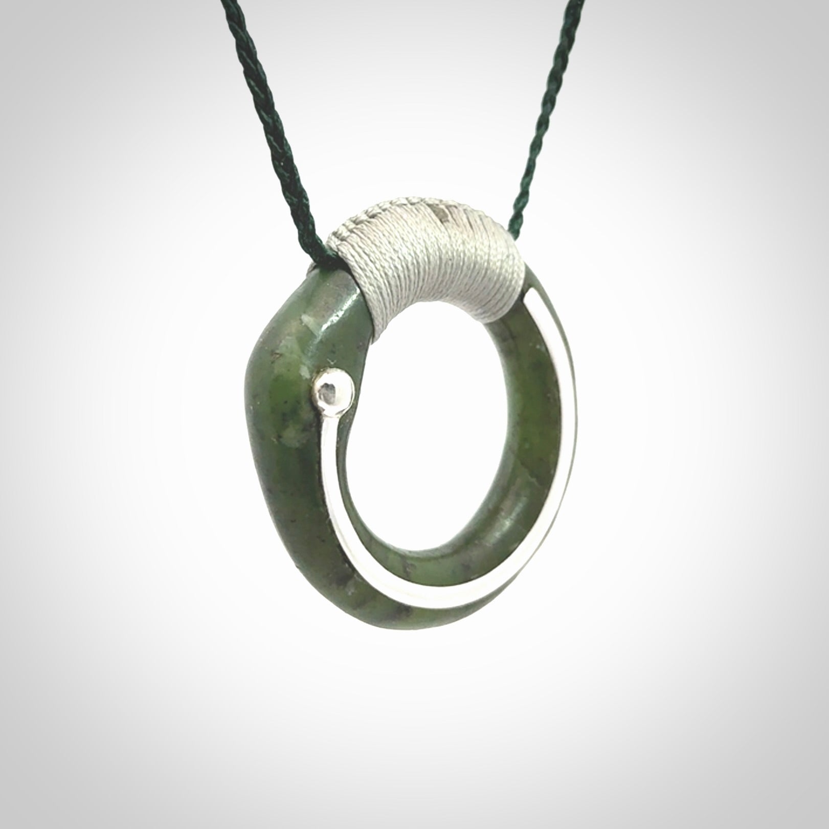 This picture shows a hand carved Nephrite jade circle pendant with sterling silver inlay. It is suspended from an adjustable coloured cord. Delivery is free worldwide.