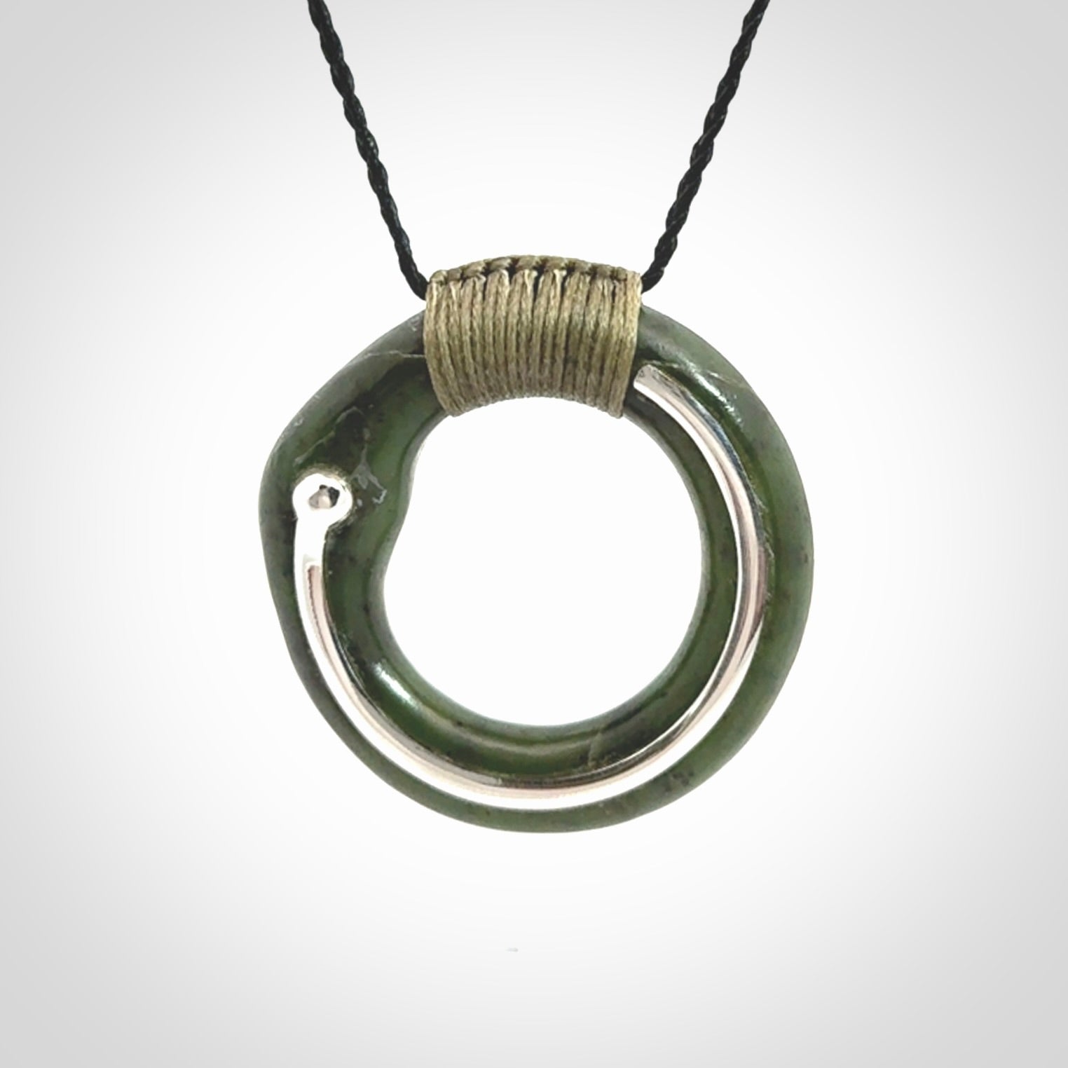This picture shows a hand carved Nephrite jade zen circle pendant with sterling silver inlay. It is suspended from an adjustable cord.