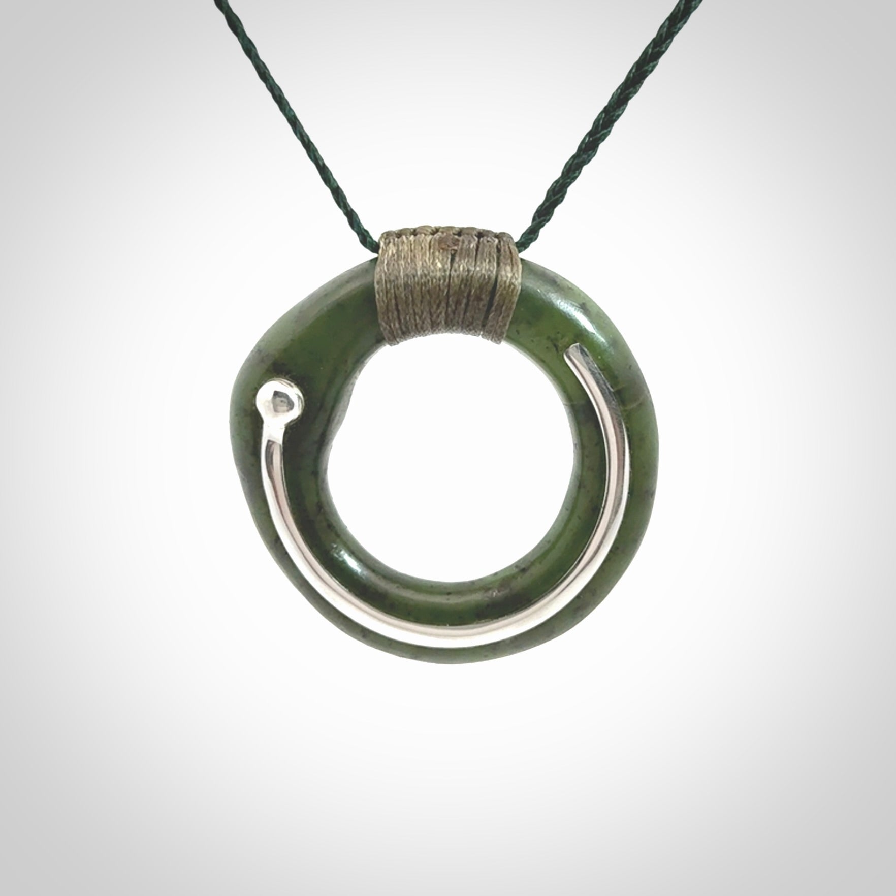 This picture shows a hand carved Nephrite jade zen circle pendant with sterling silver inlay. It is suspended from an adjustable cord.