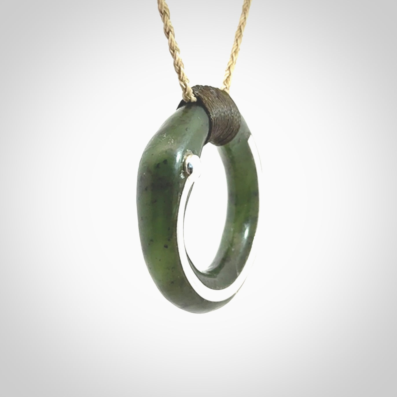 This picture shows a hand carved Nephrite jade circle pendant with sterling silver inlay. It is suspended from an adjustable Kalahari coloured cord. Delivery is free worldwide.