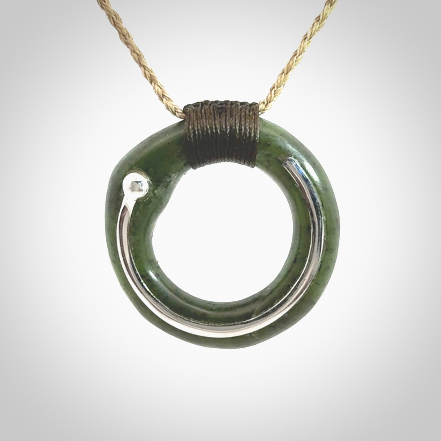 This picture shows a hand carved Nephrite jade circle pendant with sterling silver inlay. It is suspended from an adjustable Kalahari coloured cord. Delivery is free worldwide.