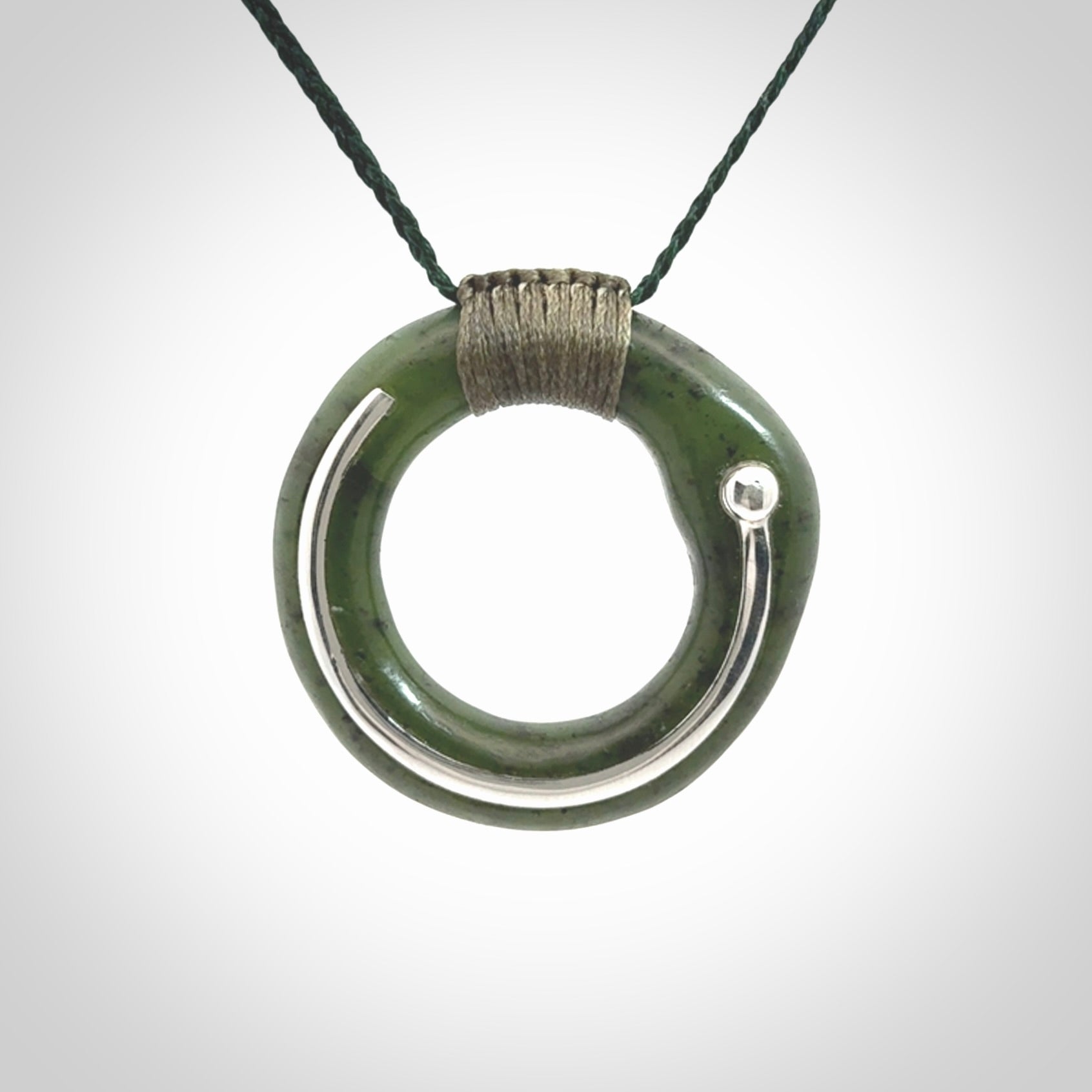 This picture shows a hand carved Nephrite jade zen circle pendant with sterling silver inlay. It is suspended from an adjustable cord.
