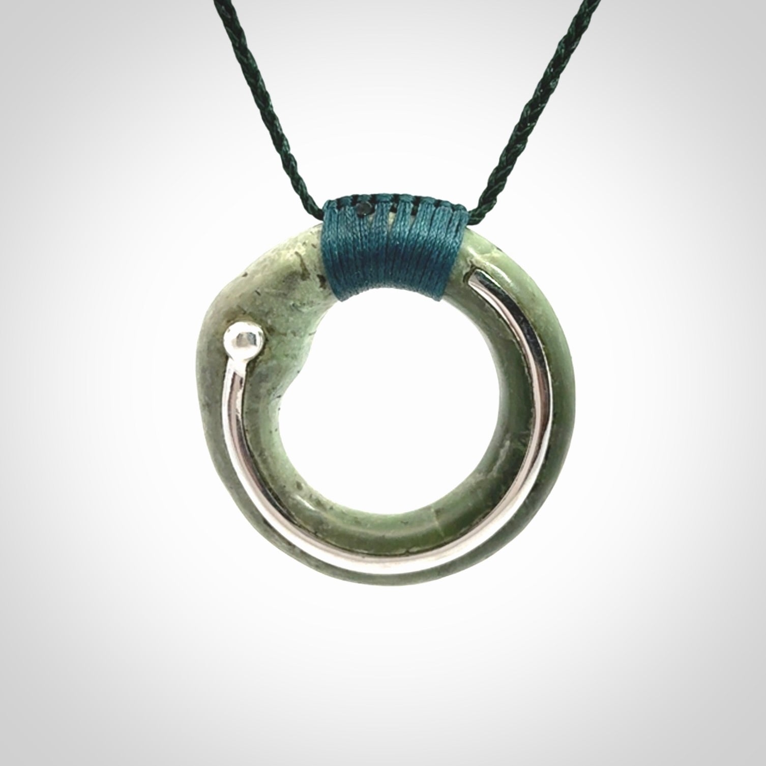 This picture shows a hand carved Nephrite jade zen circle pendant with sterling silver inlay. It is suspended from an adjustable cord.