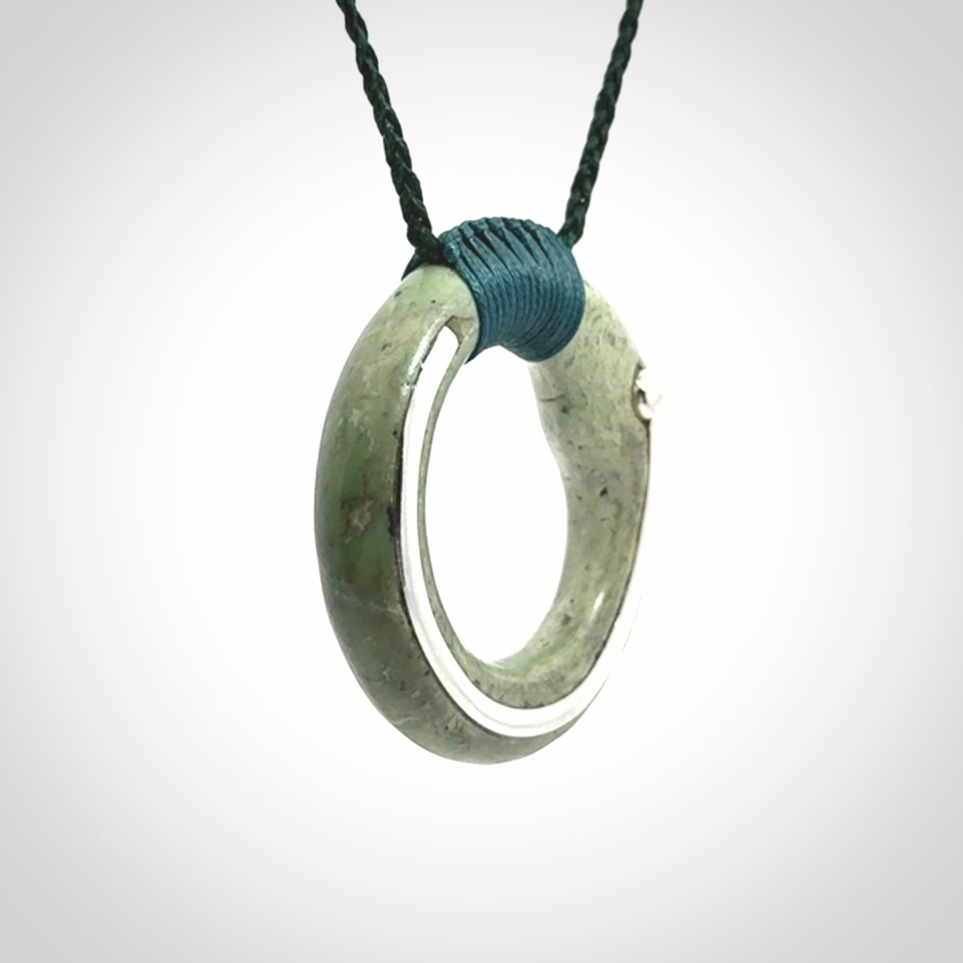 This picture shows a hand carved Nephrite jade zen circle pendant with sterling silver inlay. It is suspended from an adjustable cord.