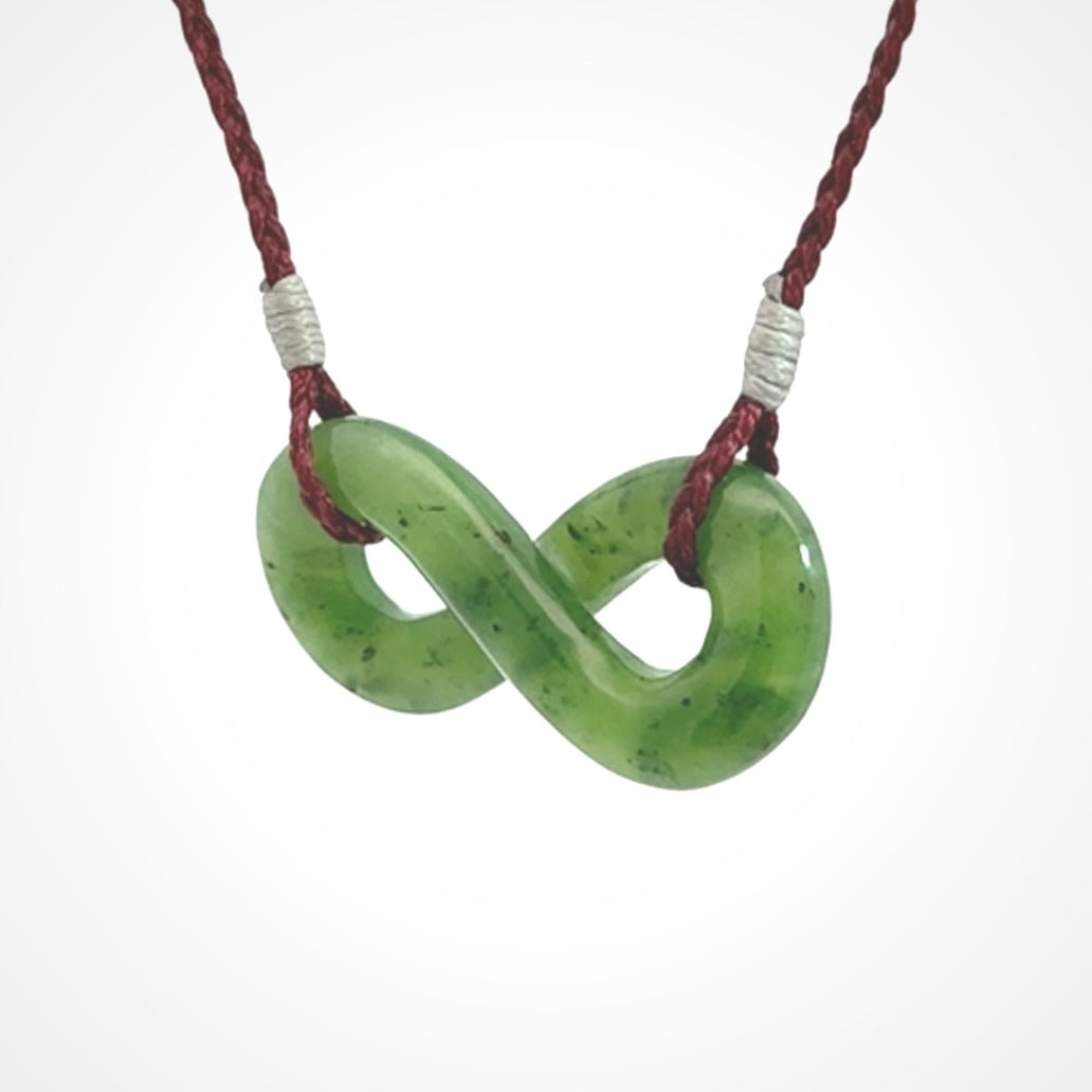 This piece is a fine, delicate eternity shaped pendant. It was carved from a lovely green piece of British Columbian jade. It is suspended on an plum coloured cord that is length adjustable.