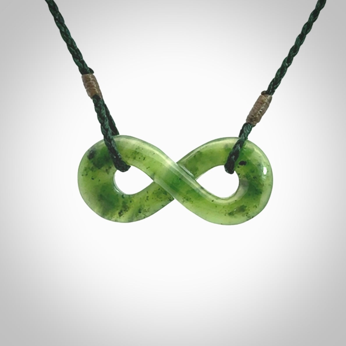 This piece is a fine, delicate eternity shaped pendant. It was carved from a lovely green piece of British Columbian jade. It is suspended on an green coloured cord that is length adjustable.
