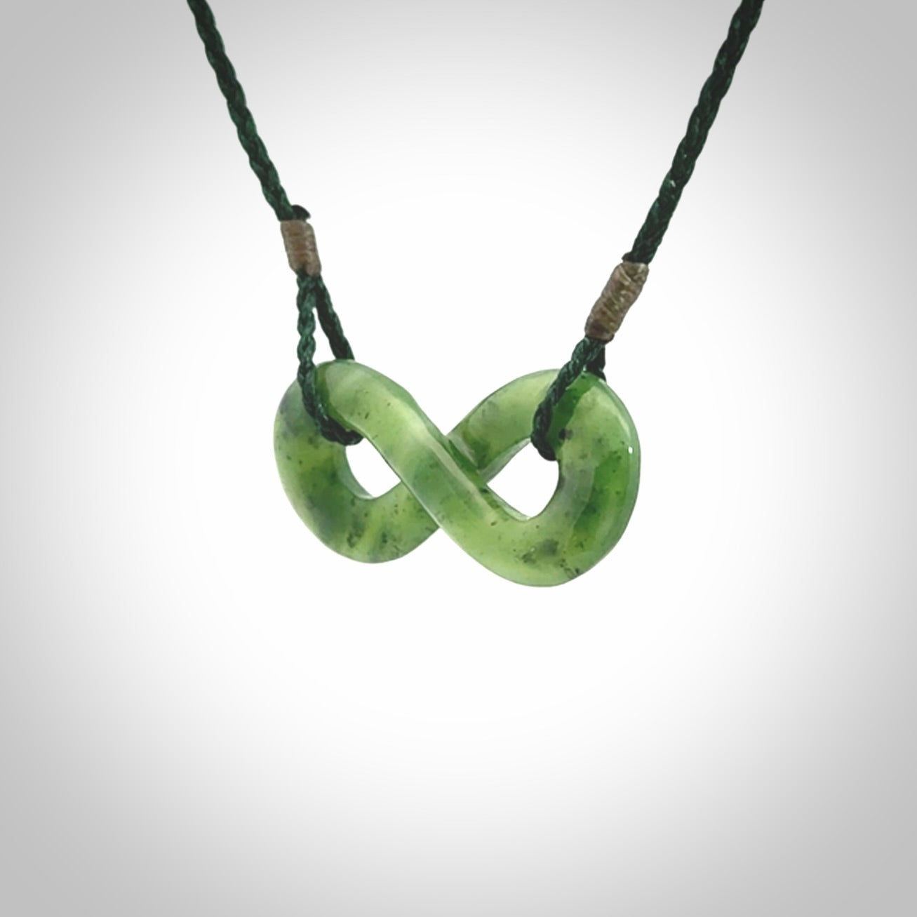 This piece is a fine, delicate eternity shaped pendant. It was carved from a lovely green piece of British Columbian jade. It is suspended on an green coloured cord that is length adjustable.