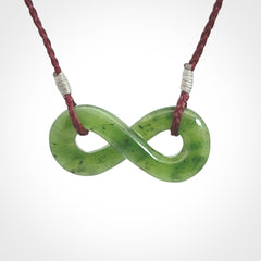 This piece is a fine, delicate eternity shaped pendant. It was carved from a lovely green piece of British Columbian jade. It is suspended on an plum coloured cord that is length adjustable.