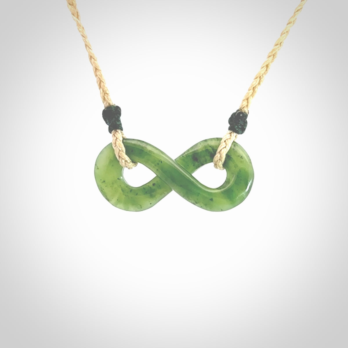This piece is a fine, delicate eternity shaped pendant. It was carved from a lovely green piece of British Columbian jade. It is suspended on an oat coloured cord that is length adjustable.