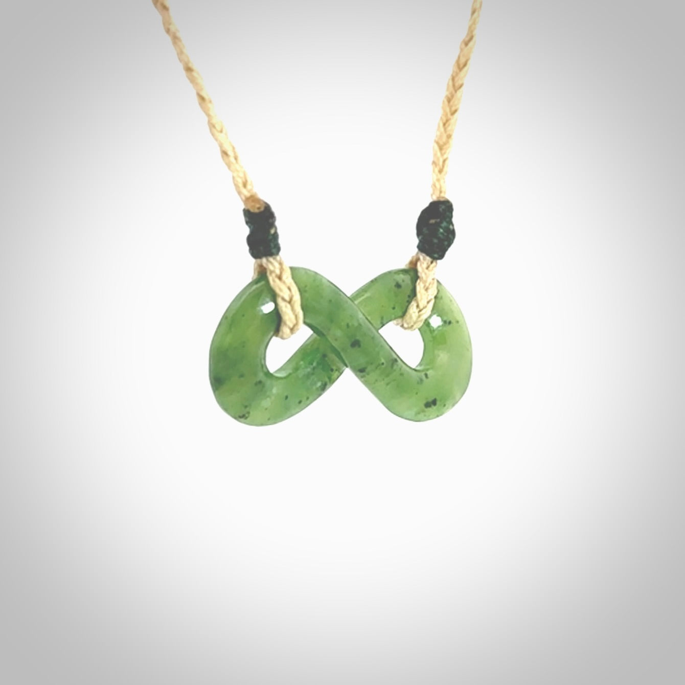 This piece is a fine, delicate eternity shaped pendant. It was carved from a lovely green piece of British Columbian jade. It is suspended on an oat coloured cord that is length adjustable.