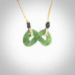 This piece is a fine, delicate eternity shaped pendant. It was carved from a lovely green piece of British Columbian jade. It is suspended on an oat coloured cord that is length adjustable.