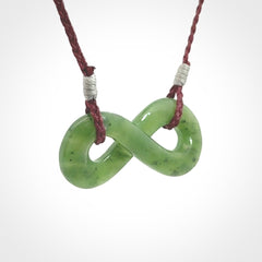 This piece is a fine, delicate eternity shaped pendant. It was carved from a lovely green piece of British Columbian jade. It is suspended on an plum coloured cord that is length adjustable.