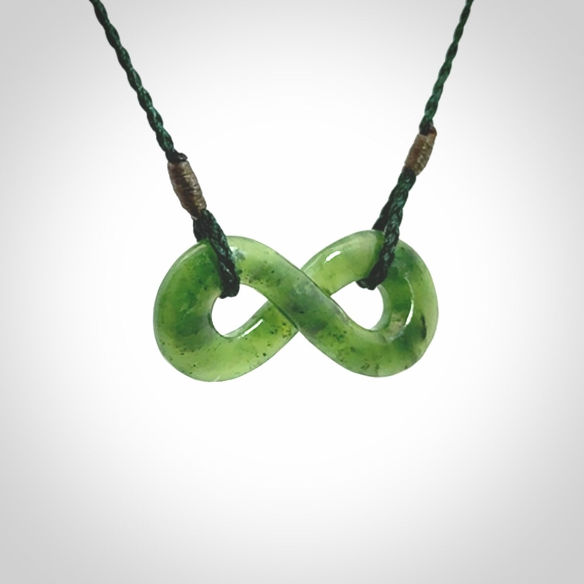 This piece is a fine, delicate eternity shaped pendant. It was carved from a lovely green piece of British Columbian jade. It is suspended on an green coloured cord that is length adjustable.