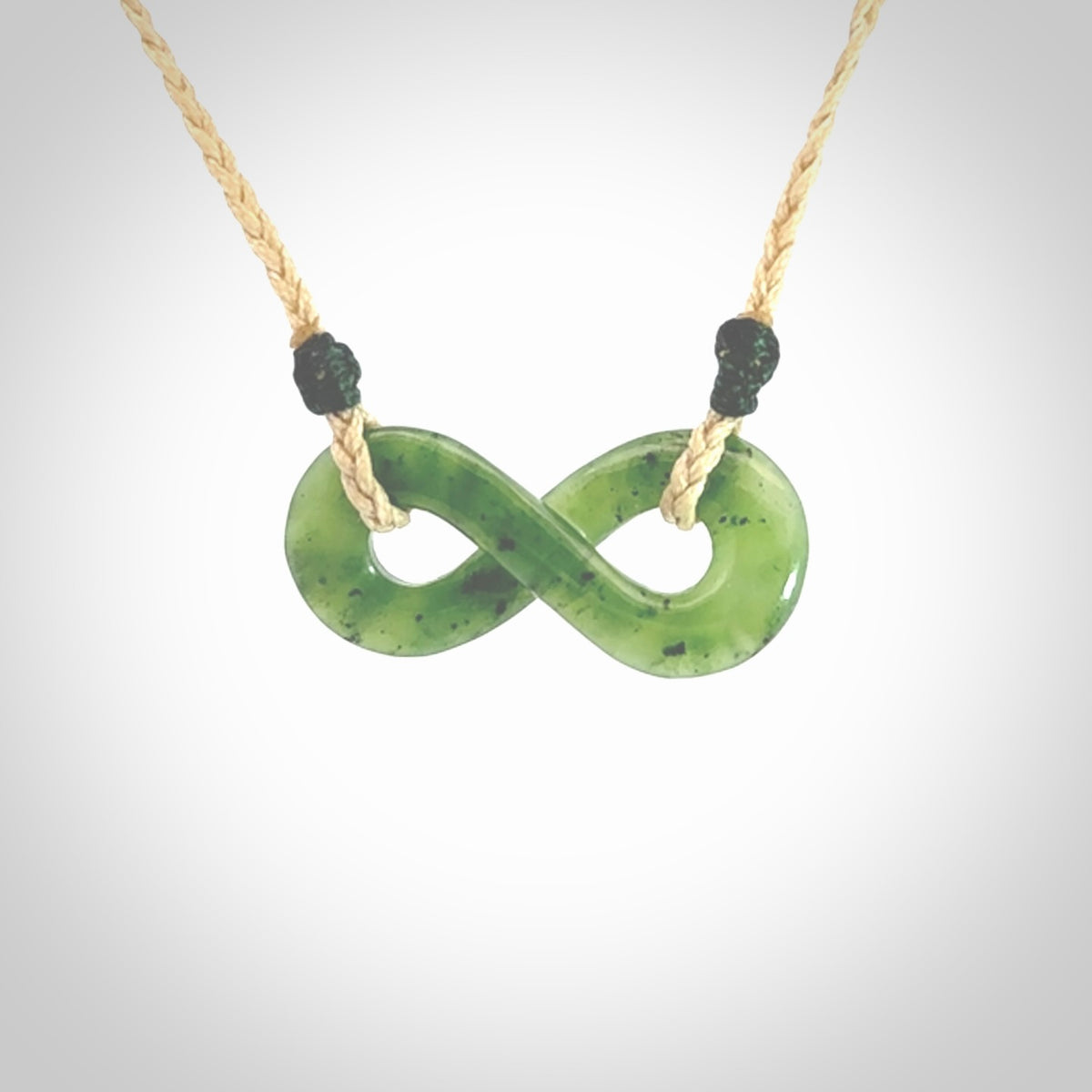 This piece is a fine, delicate eternity shaped pendant. It was carved from a lovely green piece of British Columbian jade. It is suspended on an oat coloured cord that is length adjustable.