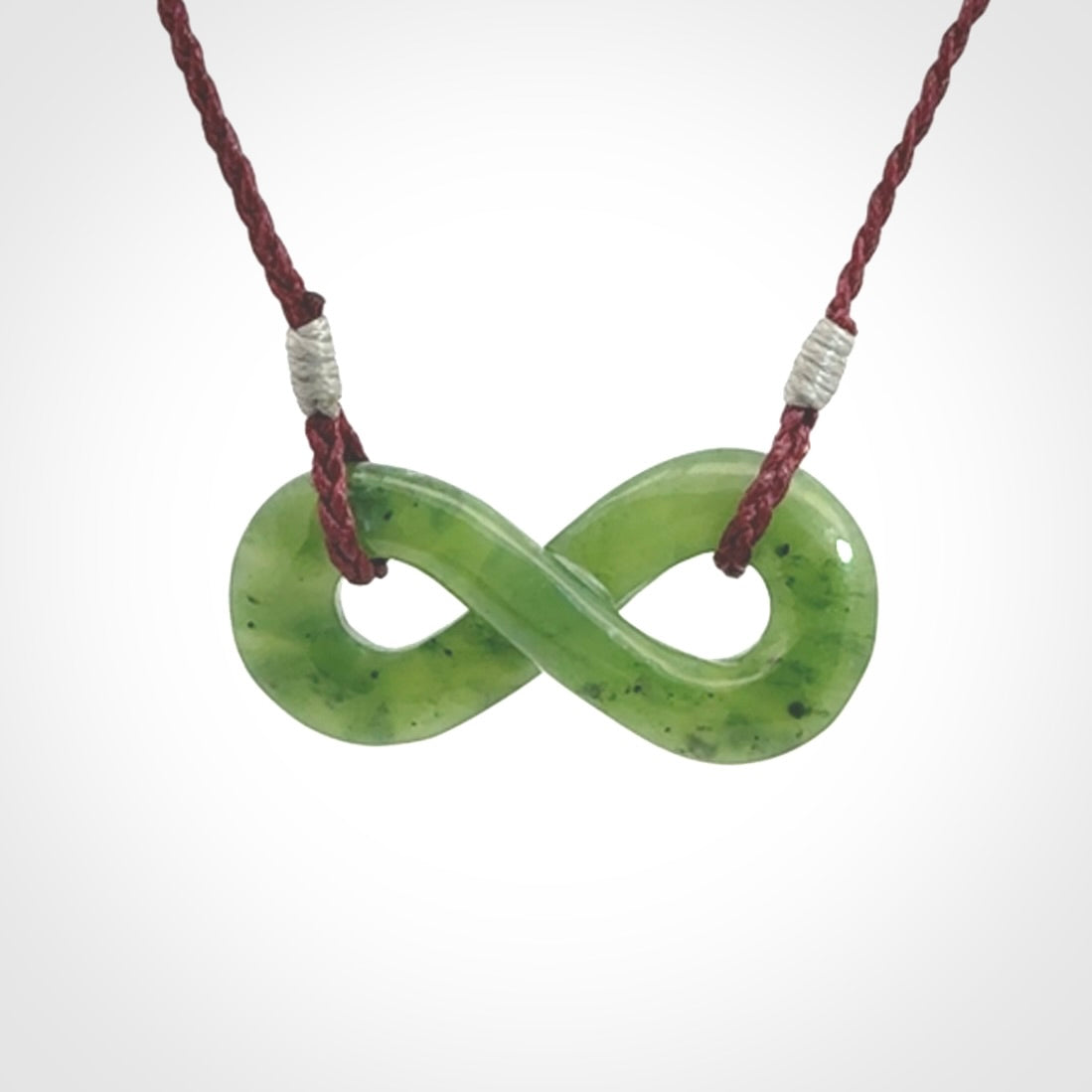 This piece is a fine, delicate eternity shaped pendant. It was carved from a lovely green piece of British Columbian jade. It is suspended on an plum coloured cord that is length adjustable.