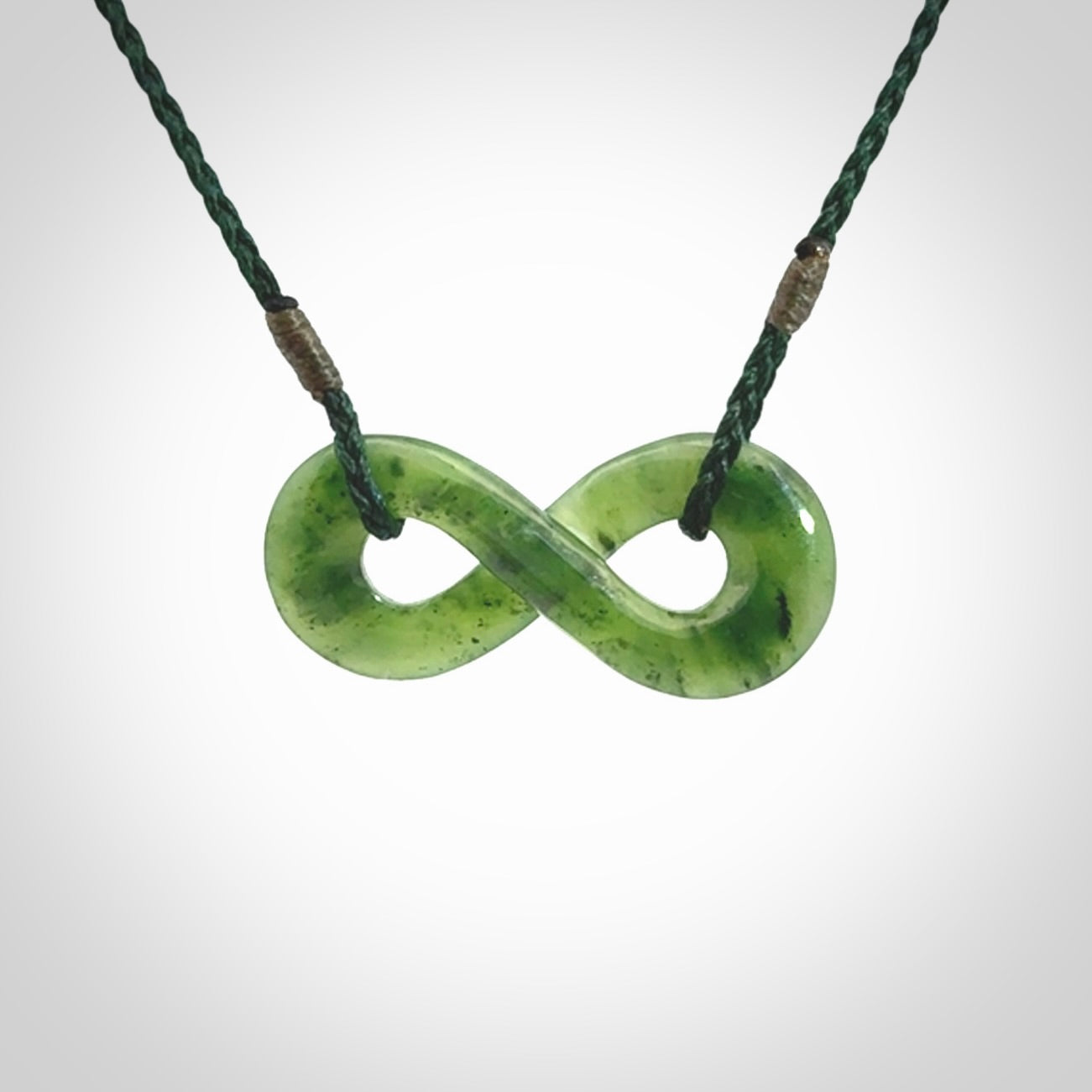 This piece is a fine, delicate eternity shaped pendant. It was carved from a lovely green piece of British Columbian jade. It is suspended on an green coloured cord that is length adjustable.