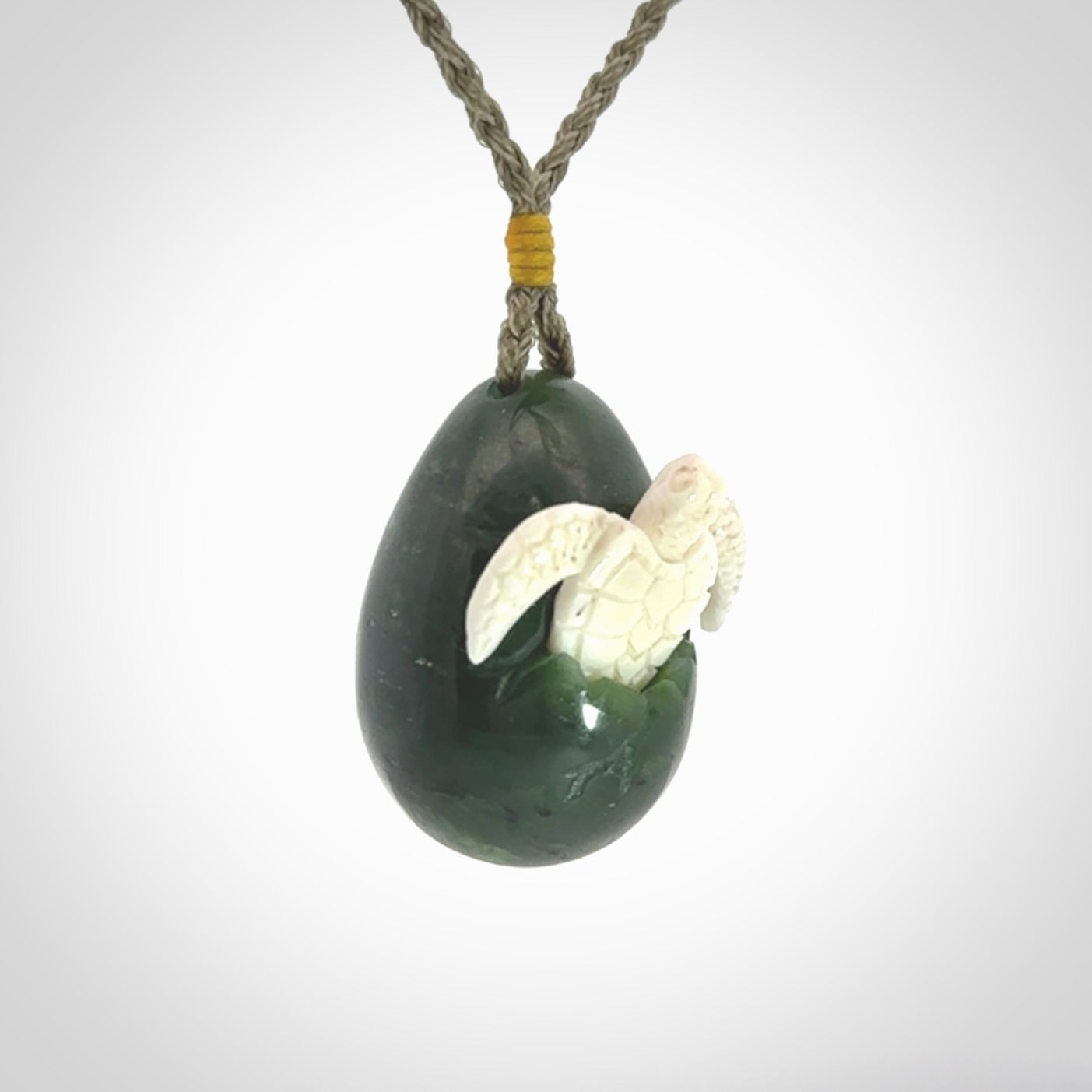 Hand carved turtle hatchling pendant. The egg is carved from green British Columbian jade and the turtle from bone. Designed and carved by NZ Pacific and for sale online.