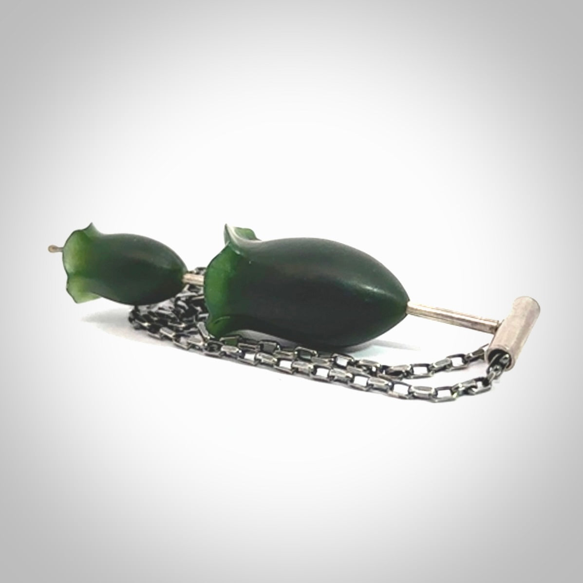 This is a very dark green flower bud pendant carved here in New Zealand by Josey Coyle. It is handmade carved jade double flower buds one placed above the other on a fine silver wire. The top is a T-shaped tube through which a silver necklace chain passes. The jade florets are handcarved from beautiful dark green New Zealand Marsden Jade and the chain is handmade from sterling silver wire.