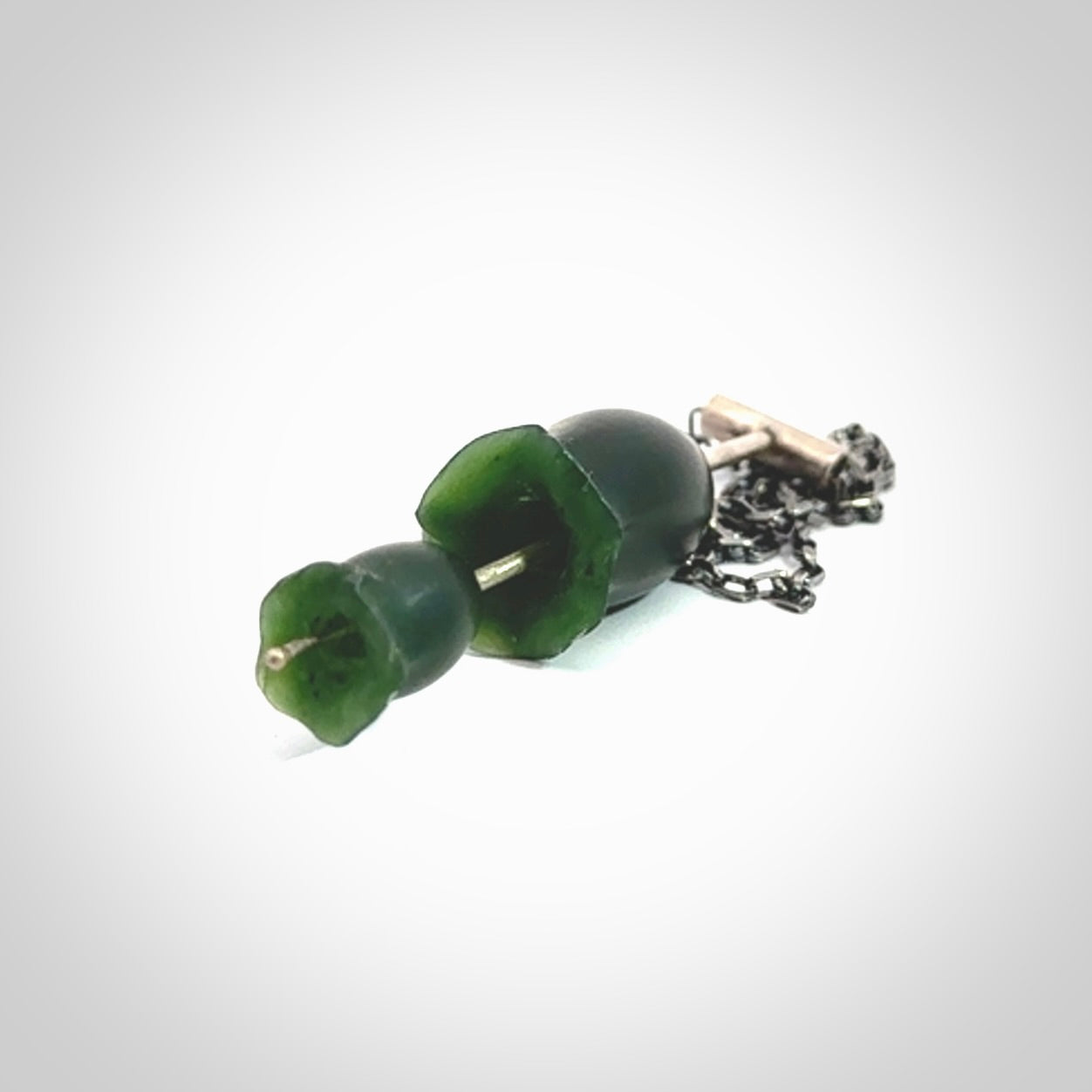 This is a very dark green flower bud pendant carved here in New Zealand by Josey Coyle. It is handmade carved jade double flower buds one placed above the other on a fine silver wire. The top is a T-shaped tube through which a silver necklace chain passes. The jade florets are handcarved from beautiful dark green New Zealand Marsden Jade and the chain is handmade from sterling silver wire.