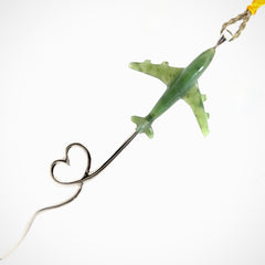 Green airplane-shaped toy hanging from a string on a white background