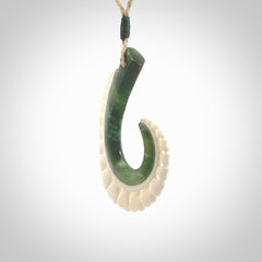 This photo shows a beautiful jade hook with bone pendant. It is handcarved from a piece of mottled green Jade, with fascinating mauve tinges through the stone. We have this on a adjustable cord. We ship this worldwide with an express courier service. Postage is free.