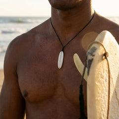 Man holding a surfboard with a necklace on a beach