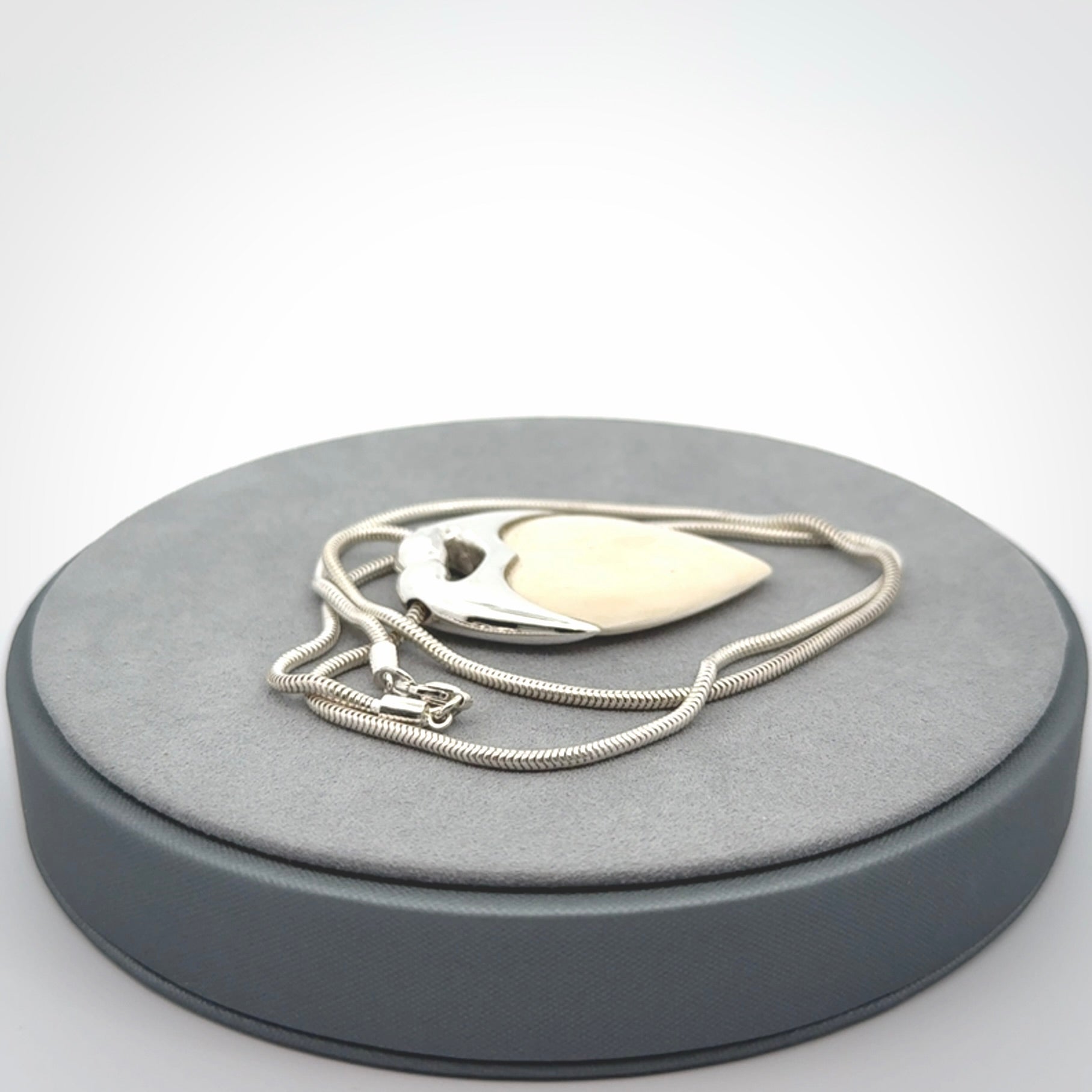 This picture shows a pendant that we have carved in a combination of sterling silver and woolly mammoth. It shows a symbolic kiss, with two heads coming together and both embracing a woolly mammoth heart. The necklace is a sterling silver chain.