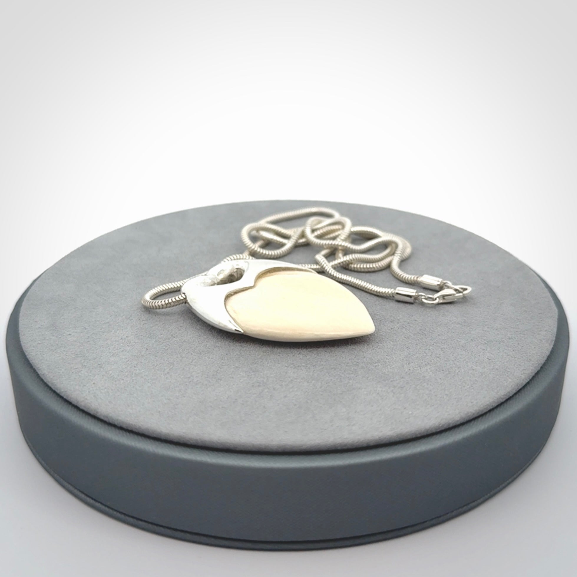 This picture shows a pendant that we have carved in a combination of sterling silver and woolly mammoth. It shows a symbolic kiss, with two heads coming together and both embracing a woolly mammoth heart. The necklace is a sterling silver chain.