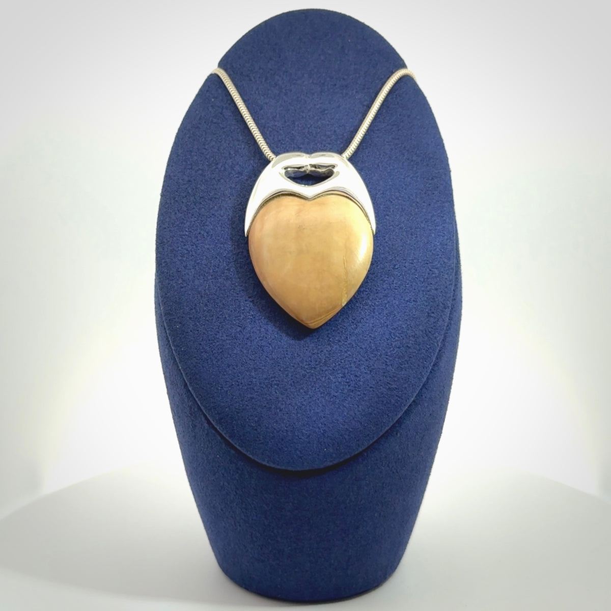 This picture shows a pendant that we have carved in a combination of sterling silver and woolly mammoth. It shows a symbolic kiss, with two heads coming together and both embracing a woolly mammoth heart. The necklace is a sterling silver chain.