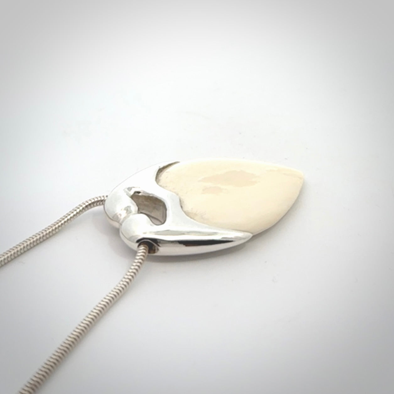 This picture shows a pendant that we have carved in a combination of sterling silver and woolly mammoth. It shows a symbolic kiss, with two heads coming together and both embracing a woolly mammoth heart. The necklace is a sterling silver chain.