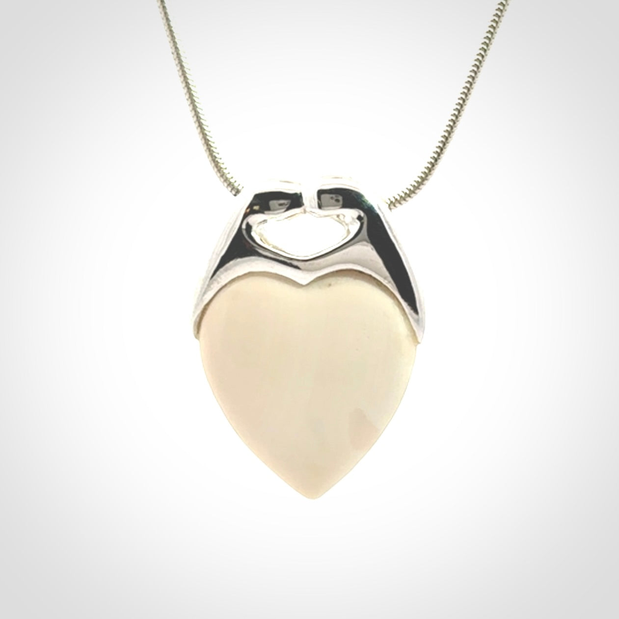 This picture shows a pendant that we have carved in a combination of sterling silver and woolly mammoth. It shows a symbolic kiss, with two heads coming together and both embracing a woolly mammoth heart. The necklace is a sterling silver chain.